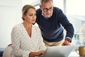 Shot of a mature couple using a laptop while going through paperwork at home